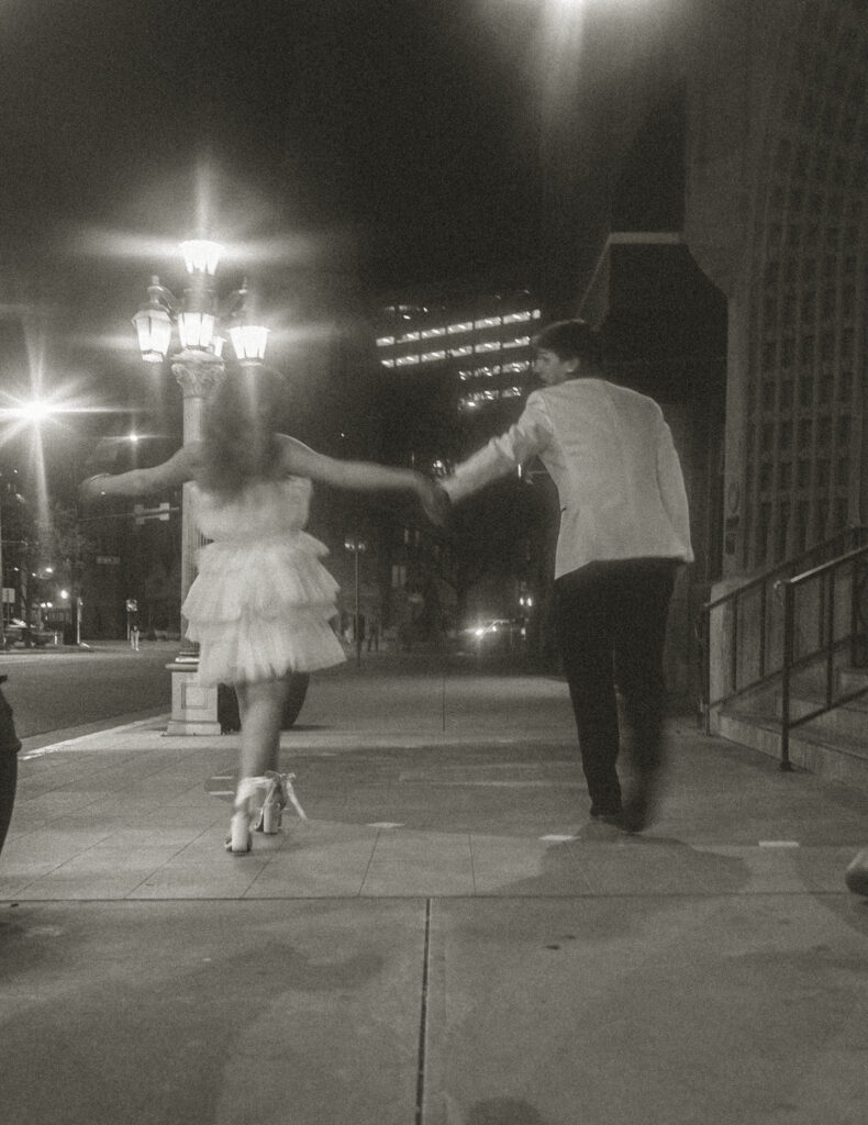 A couple stumbling down a sidewalk together on their wedding night. 