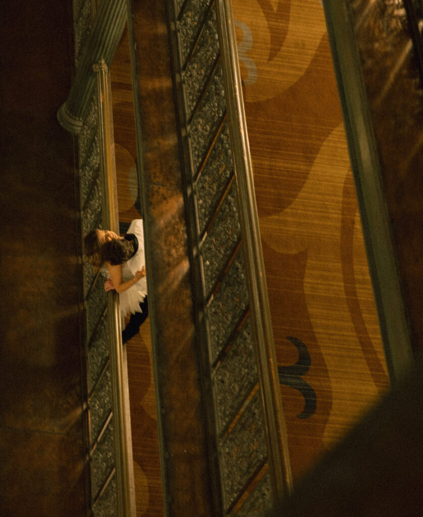 A person kissing their partners neck as they lean over a balcony. 