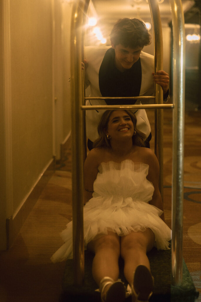 A person pushing their partner on a luggage cart in a hotel 