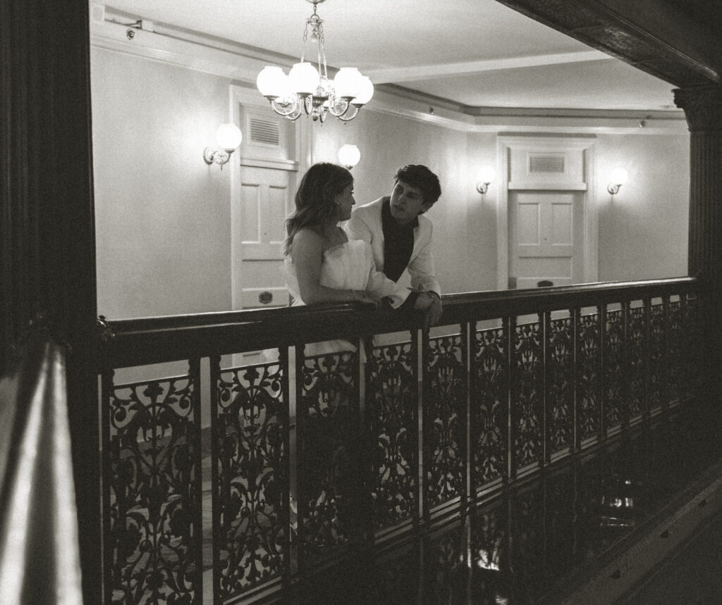 A couple leaning over a railing in a hotel talking. 