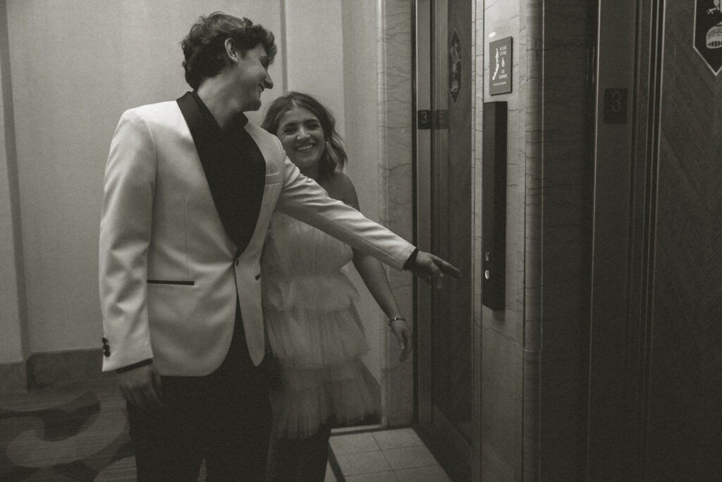 A couple laughing as one reaches for an elevator button 