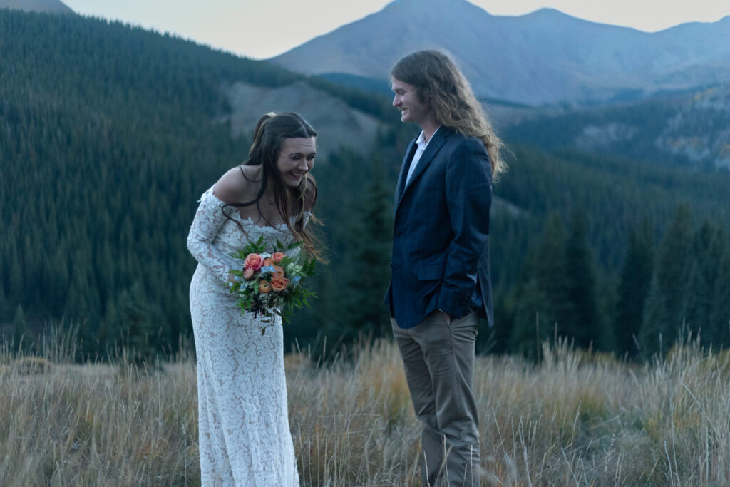 A wedding couple standing in the mountains laughing. 