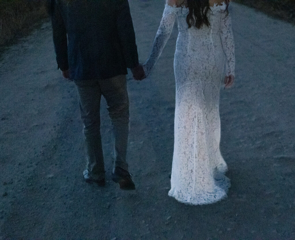 A couple holding hands and walking along a gravel road. 