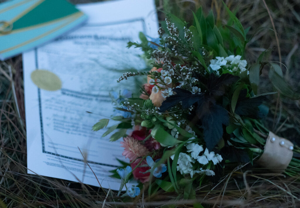 A bouquet of flowers laying on a marriage certificate in the grass. 