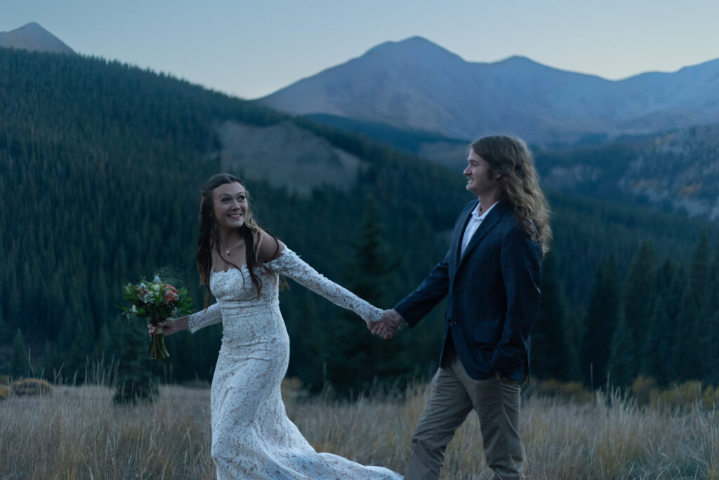 A couple holding hands and walking along a field in the mountains 