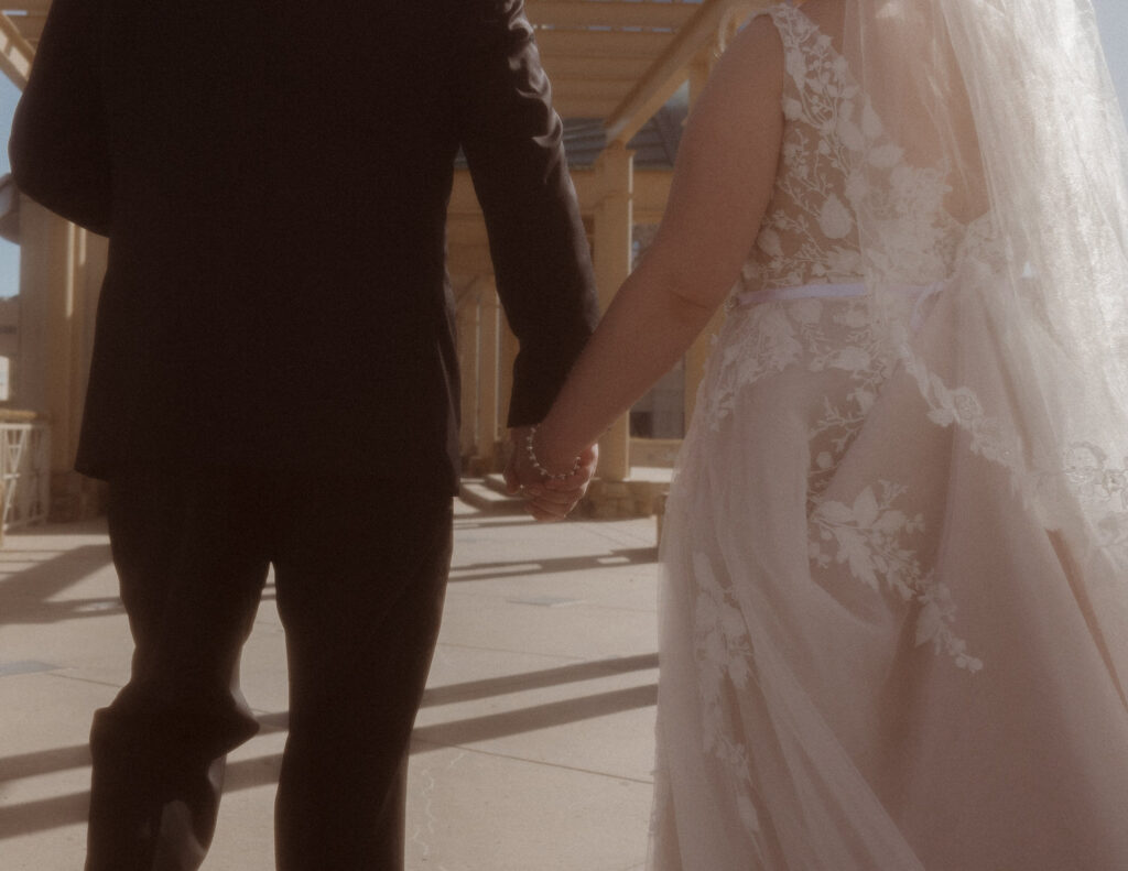 A wedding couple holding hands and walking on a sidewalk 