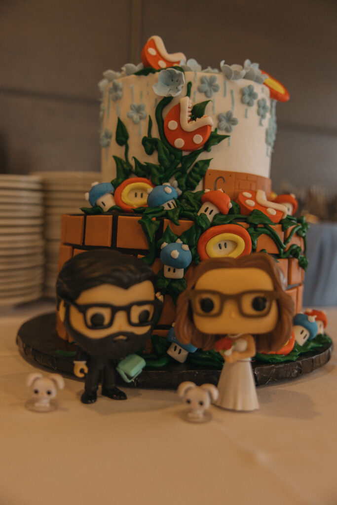 Two small figures in front of a Mario themed cake. 