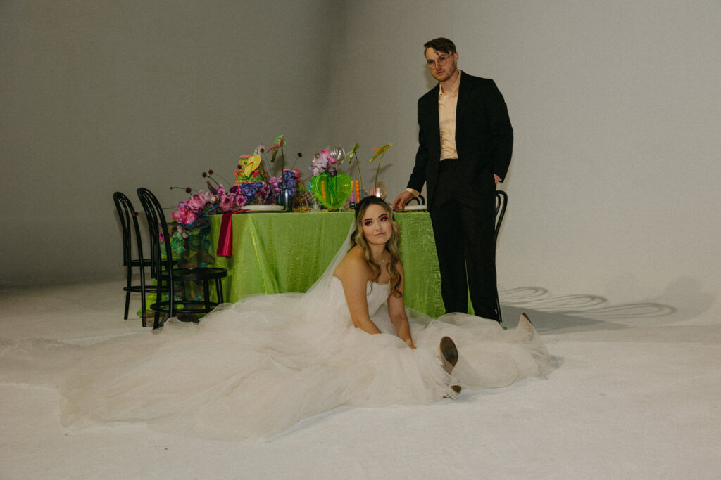 A person sitting on the floor with their dress flowing beside them as their partner stands next to them. 