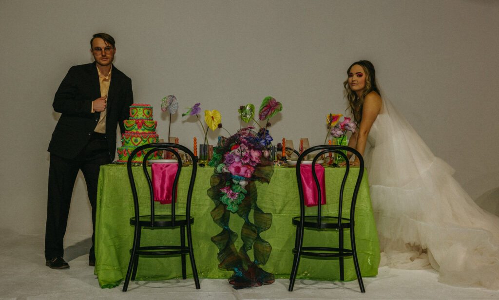 Two newlywed standing on either side of a decorated wedding reception table 