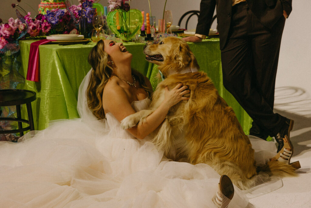 A person sitting on the ground in a wedding dress playing with a dog. 