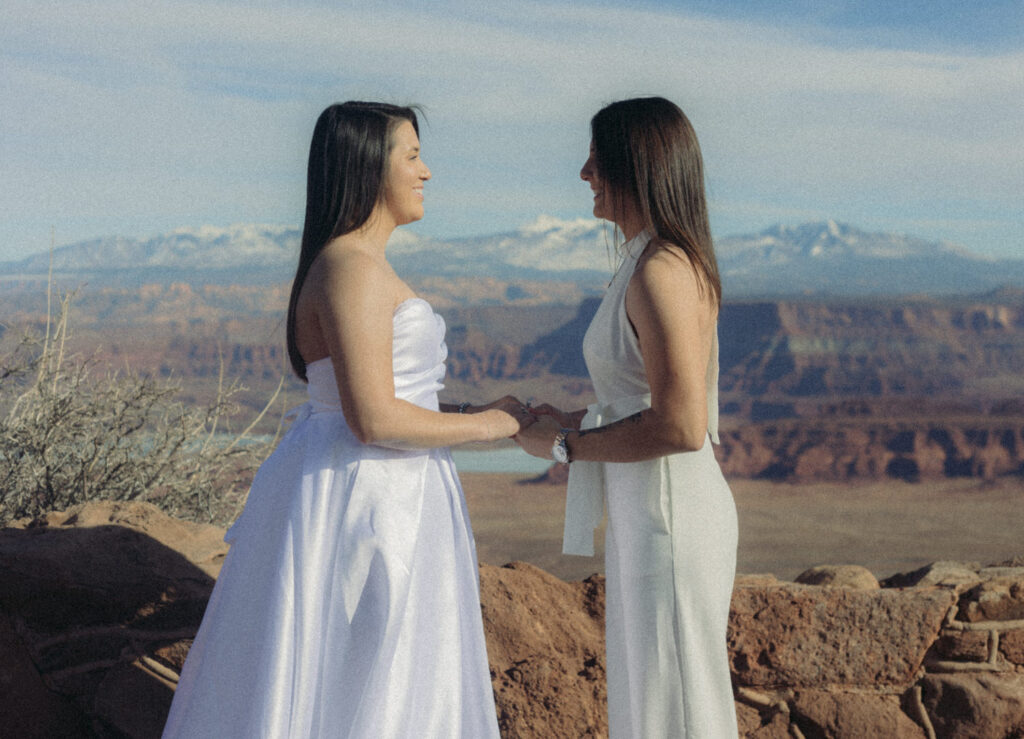 A wedding couple holding hands and smiling at each other. 