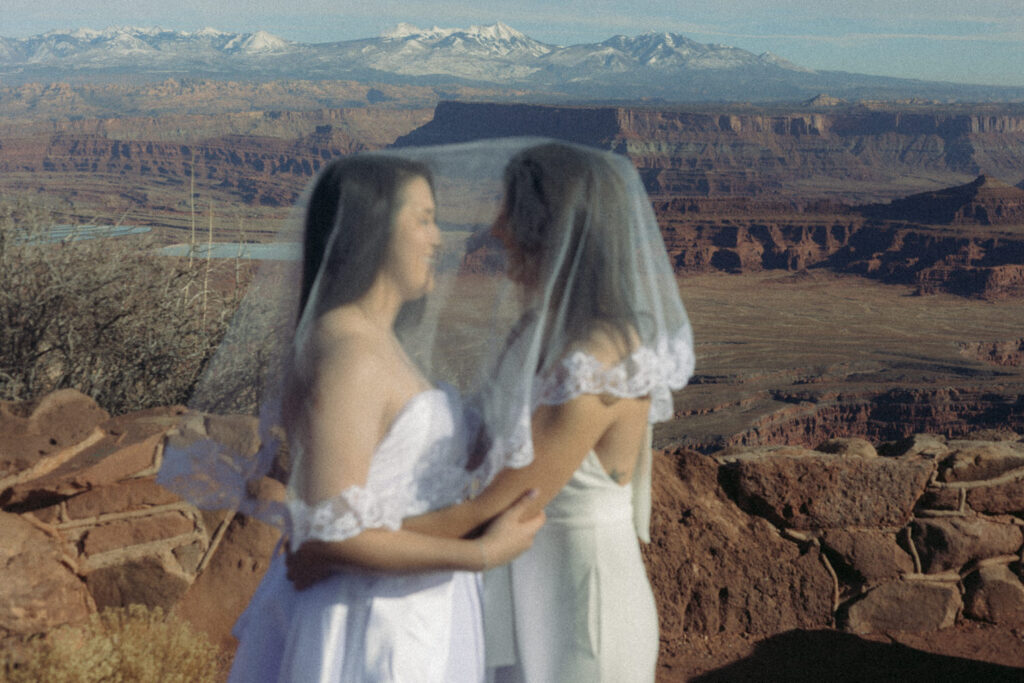 A newlywed couple holding each other while a veil is over their heads
