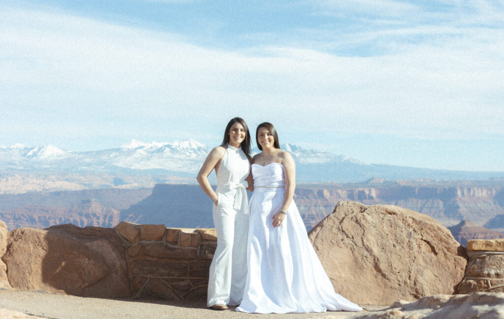 A newlywed couple standing next to them smiling with a canyon behind them 