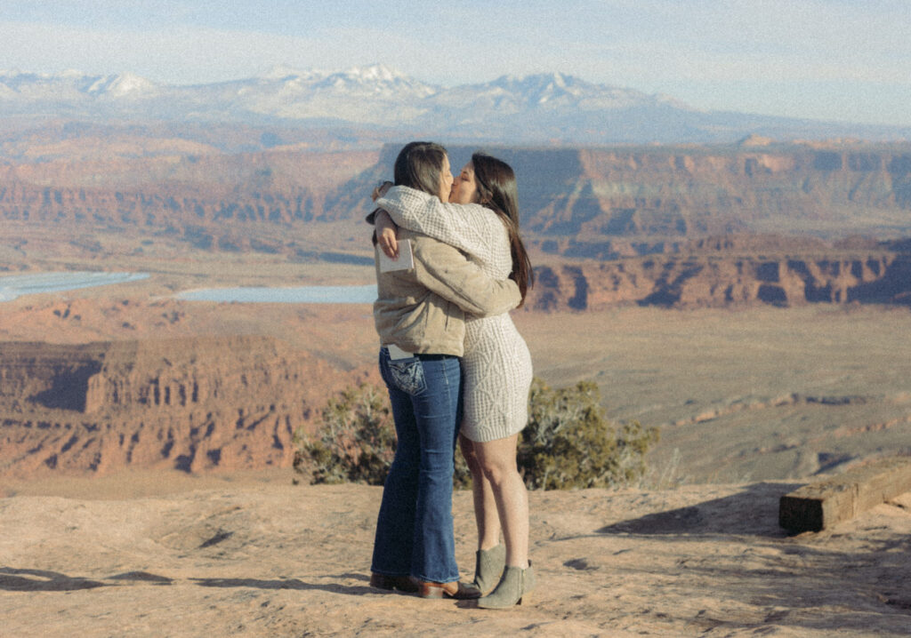 A couple hugging each other and kissing on top of a canyon. 