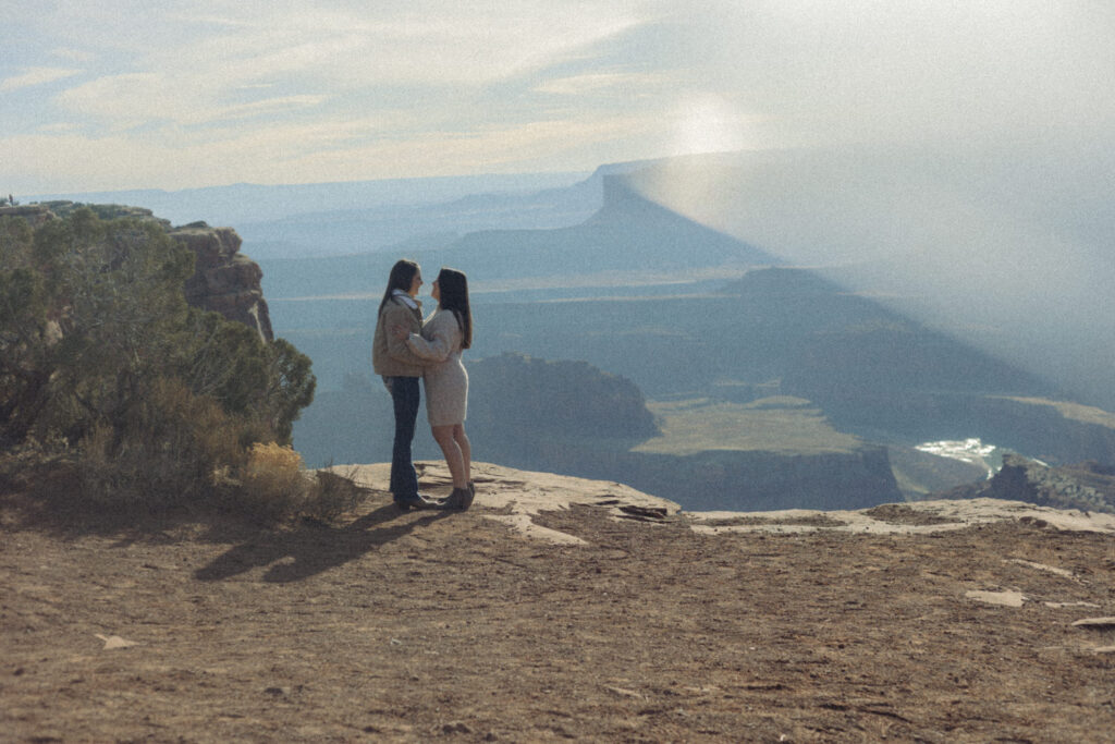 A couple standing close about to kiss with a canyon in the distance 